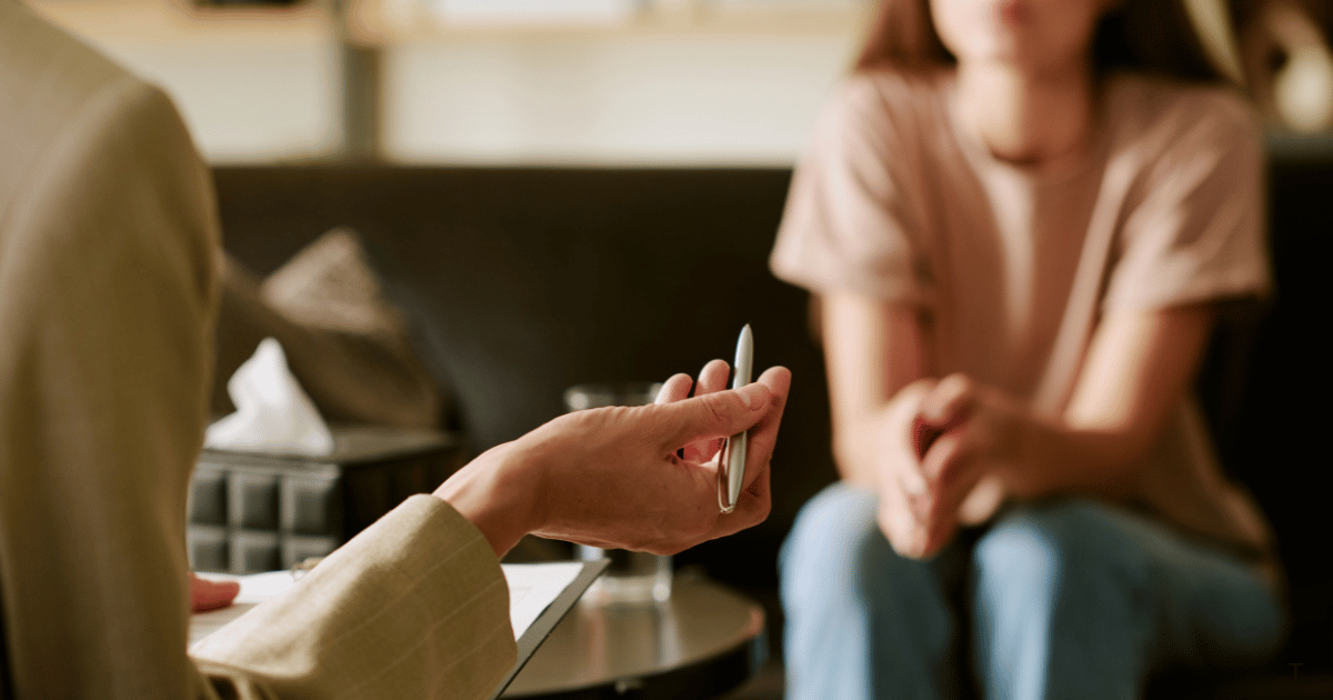 Positive young woman in casual clothes smiling while sitting on chair after psychotherapy session with anonymous female doctor in modern office
